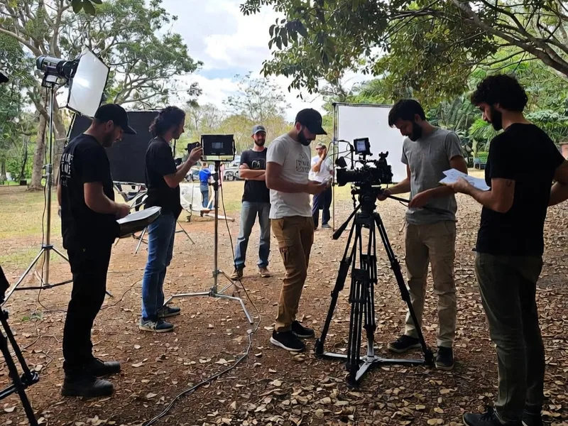 Film crew setting up a cinema camera, lights and monitors outdoors under trees in Mexico
